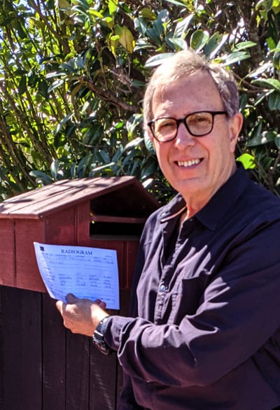 Steve ZL2KE by his letterbox holding a radiogram he received
