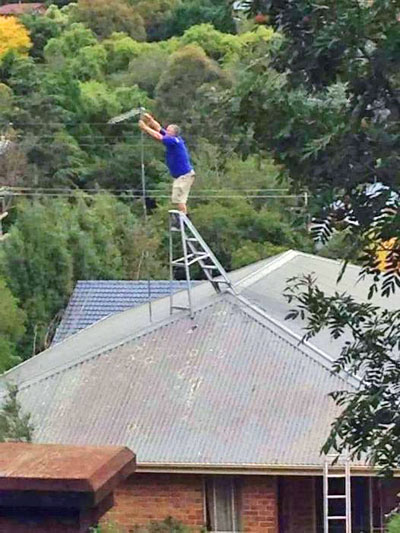 Man balanced on step ladder on top of roof to adjust TV aerial