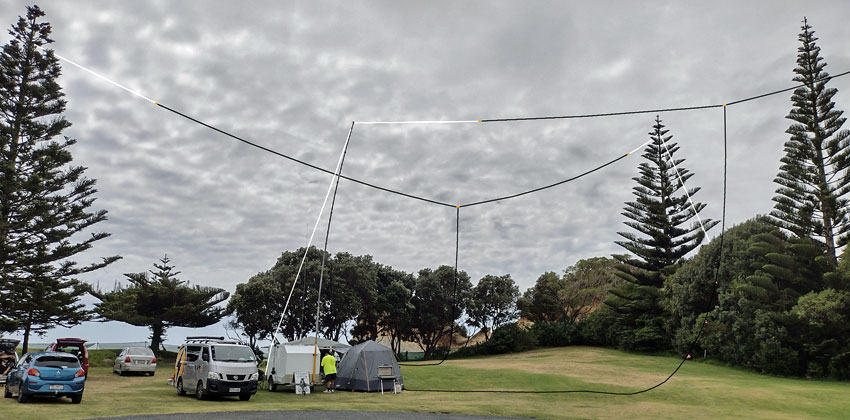 Dipoles for 80 and 40 metres strung between Norfolk Pine trees, with tents and cars parked below.